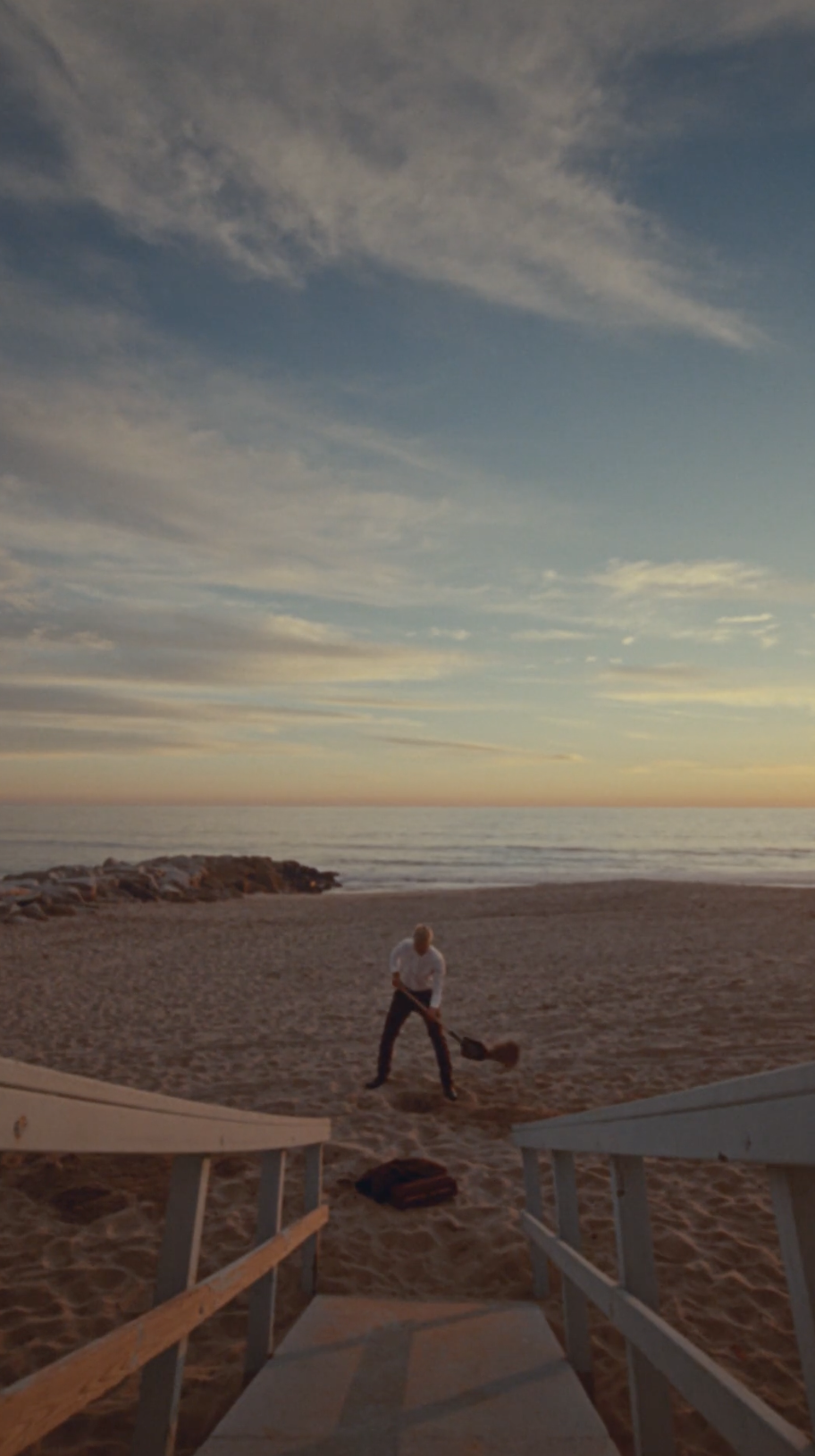 Wide shot of a figure digging on an empty beach at sunrise