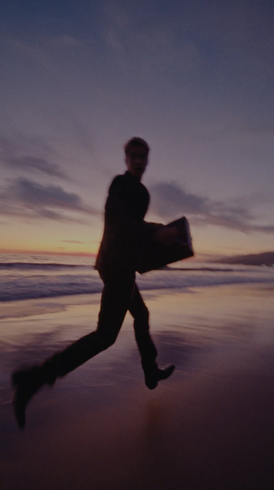 Silhouetted figure running across a beach at dusk